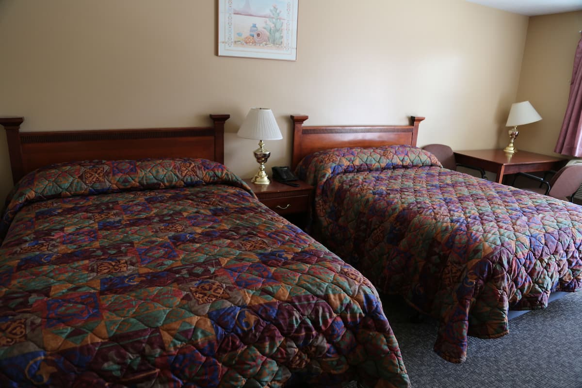 Une chambre d’hôtel avec deux lits, chacun recouvert d’une courtepointe à motifs, des tables de chevet avec des lampes et un tableau encadré au mur.