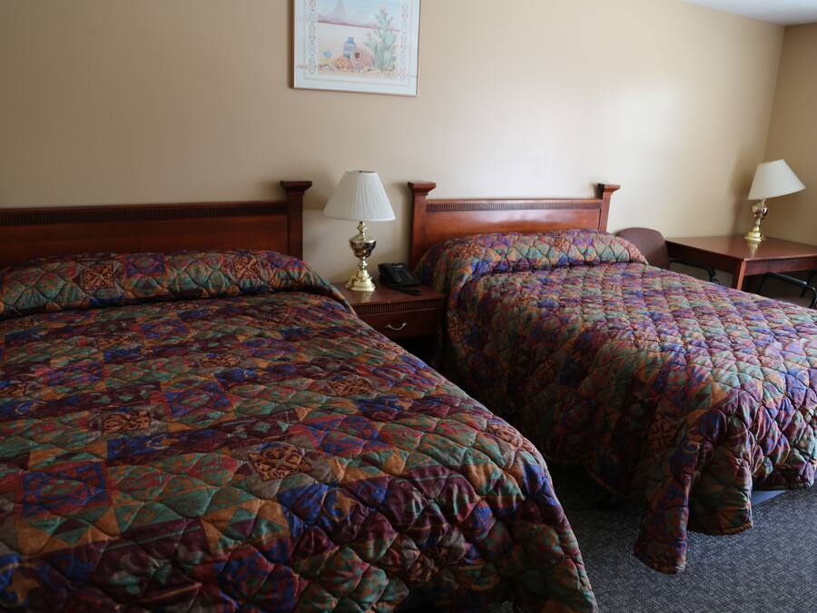 A hotel room with two beds, each with a patterned quilt, bedside tables with lamps, and a framed picture on the wall.