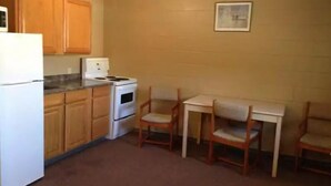 A compact kitchen with wooden cabinets, a white refrigerator, a stove, and a small dining table with chairs. - Twilite Motel & RV Park (Prince Albert)