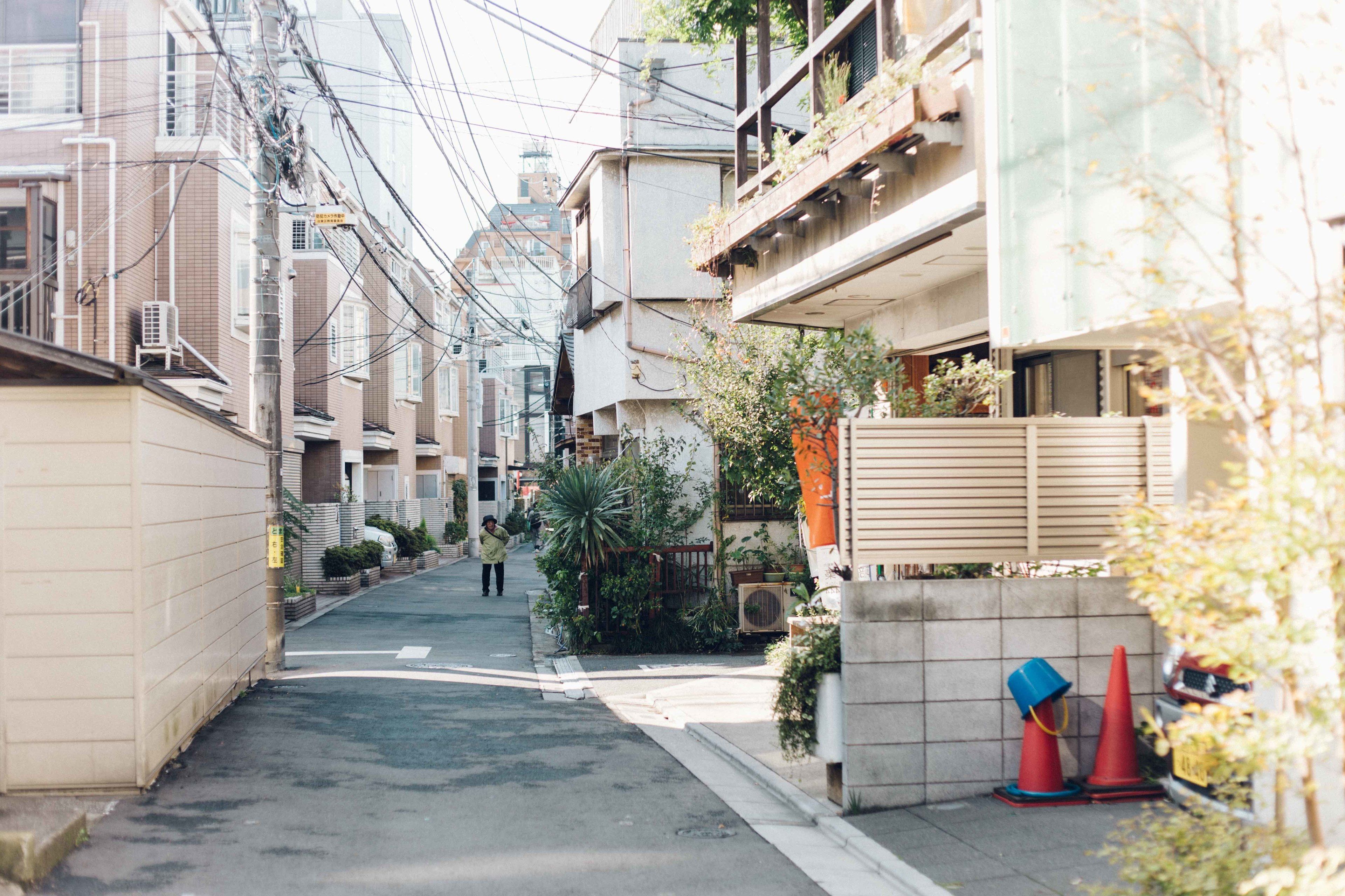 A narrow urban street lined with residential buildings, featuring a pedestrian pathway and some greenery.