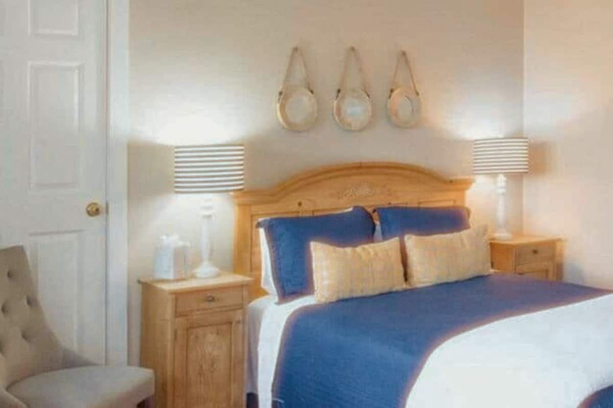 A bedroom with a bed, bedside lamps, a chair, and a painting on the wall.