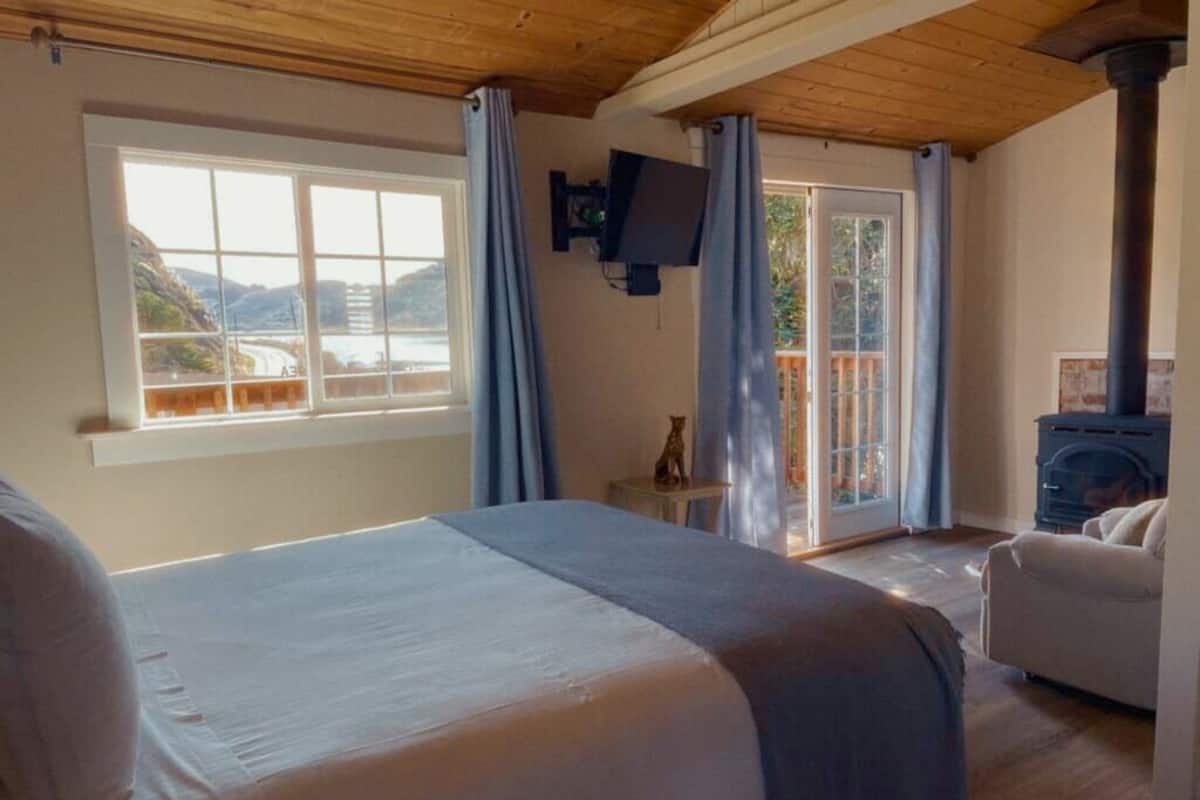 A bedroom with a large bed, a television, a fireplace, and a view of the outdoors.