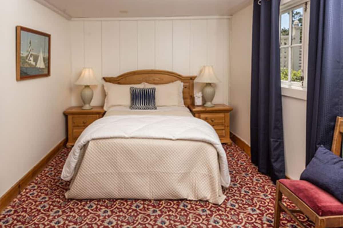 A neatly made bed with a patterned bedspread, two bedside lamps, and a window with curtains.