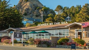 Een kustrestaurant genaamd 'Jenner by the Sea' met terras en uitzicht op een rotsheuvel.