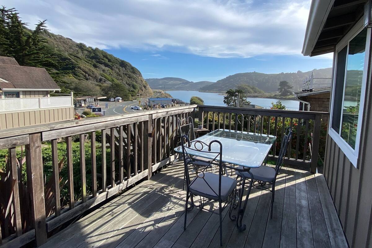 A wooden deck with a table and chairs overlooking a scenic view of hills and a body of water.