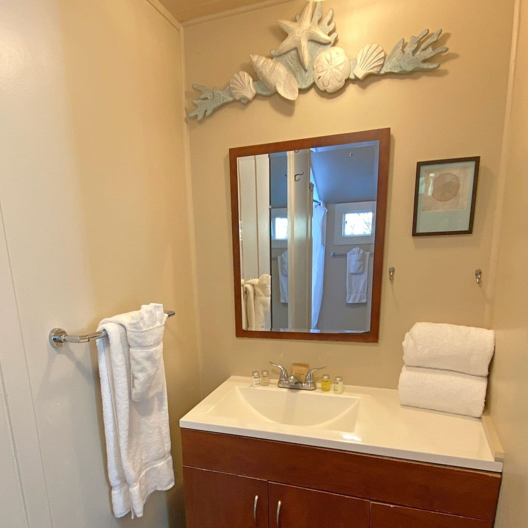 A bathroom with a white sink, a mirror, and a decorative wall piece above the mirror.