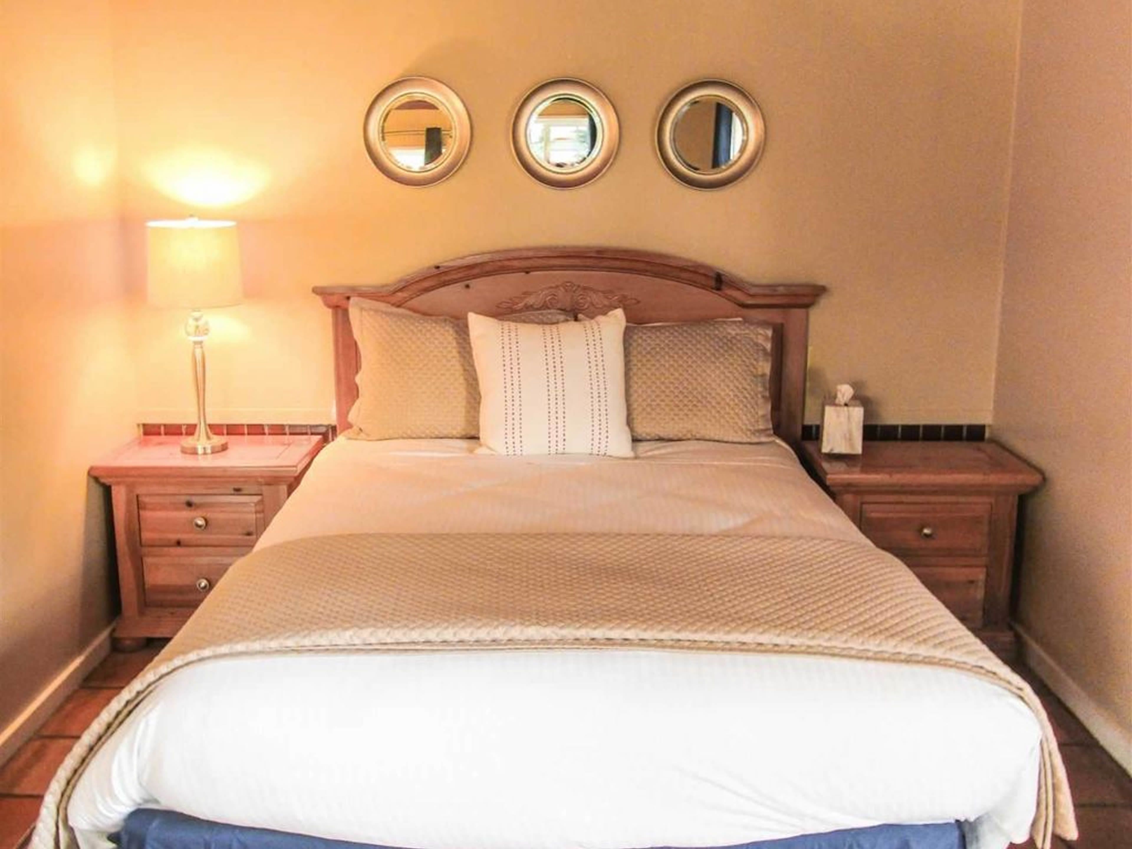 A neatly made bed with a headboard, two bedside tables with lamps, and three wall-mounted mirrors.