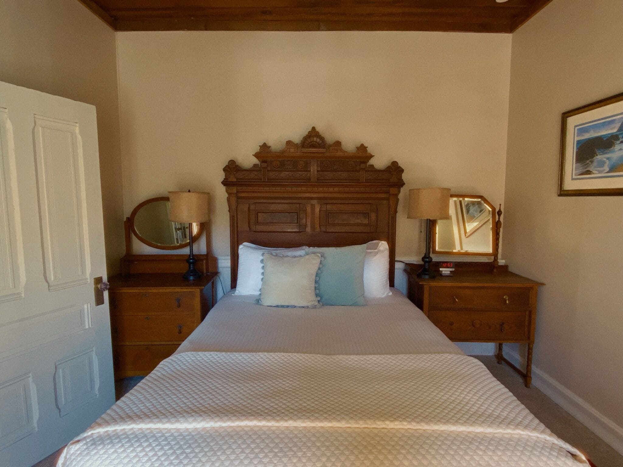 Une chambre à coucher avec un grand lit, deux tables de chevet, une tête de lit en bois et un tableau accroché au mur.