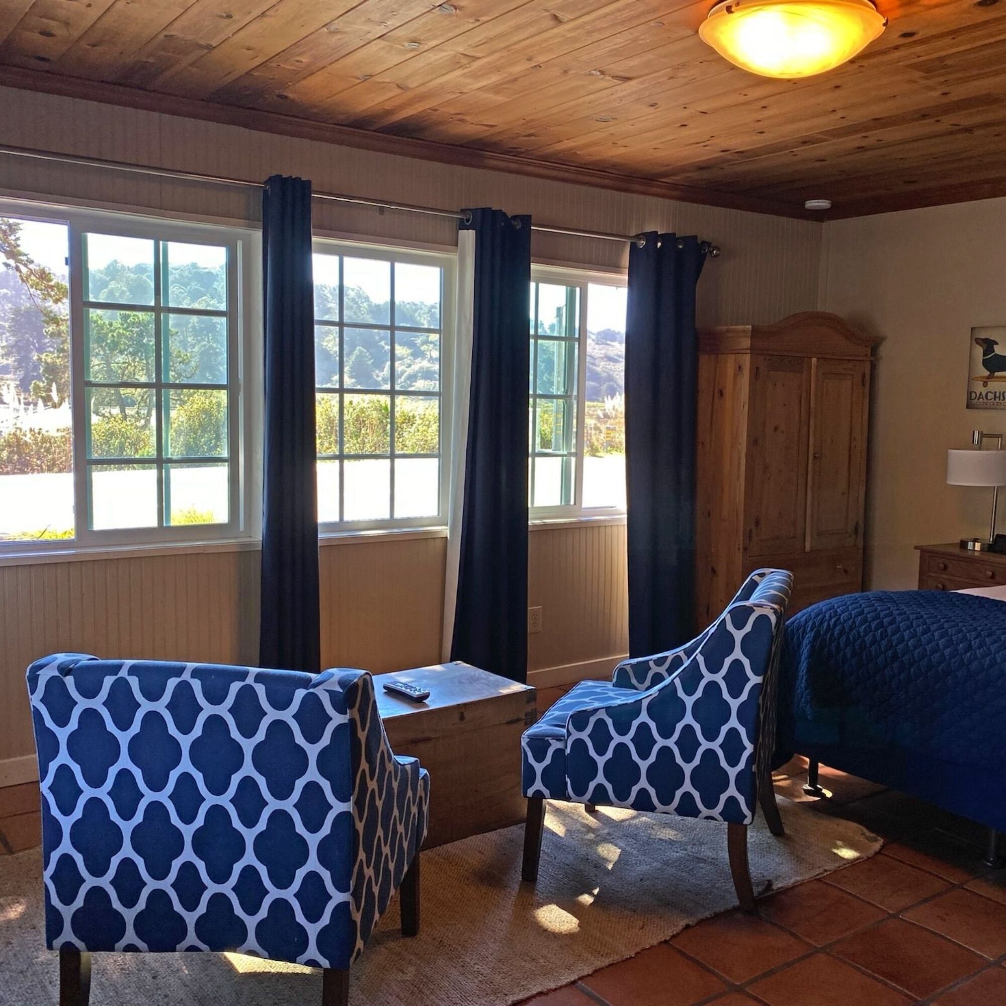A room with a bed, two patterned chairs, a small table, and a window with curtains.