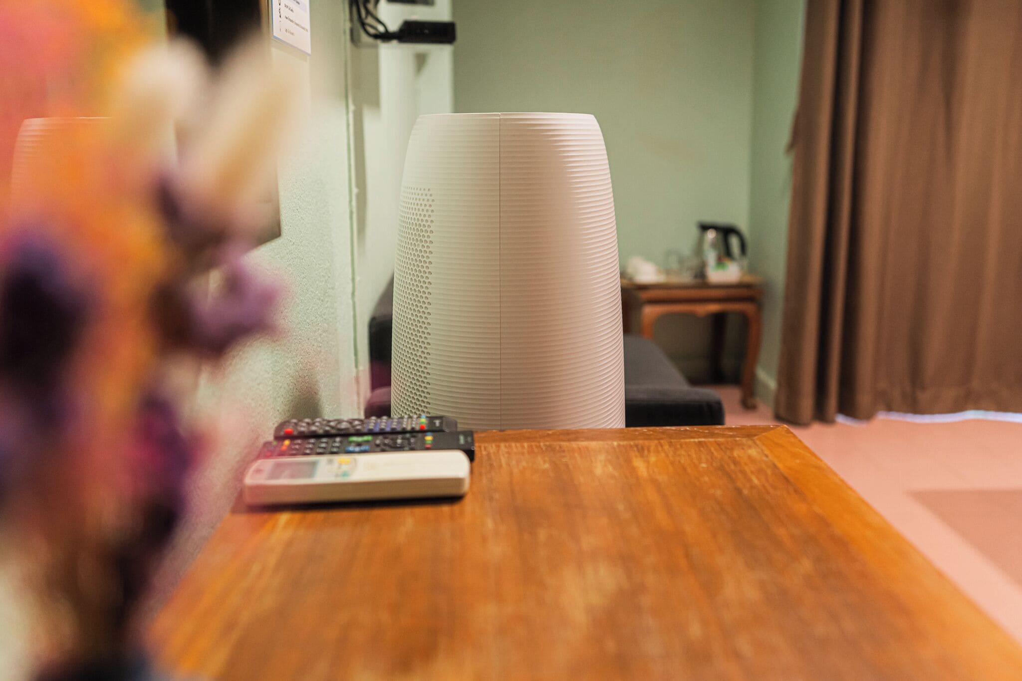 A wooden table with a remote control, a white cylindrical object, and a small table with a kettle.