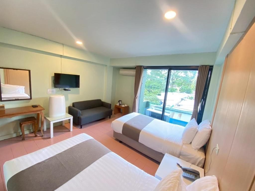 Habitación de hotel con dos camas, un escritorio, televisor y un ventanal con cortinas.