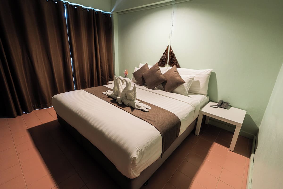 A neatly made bed with a brown headboard, a bedside table with a phone, and a window with curtains.