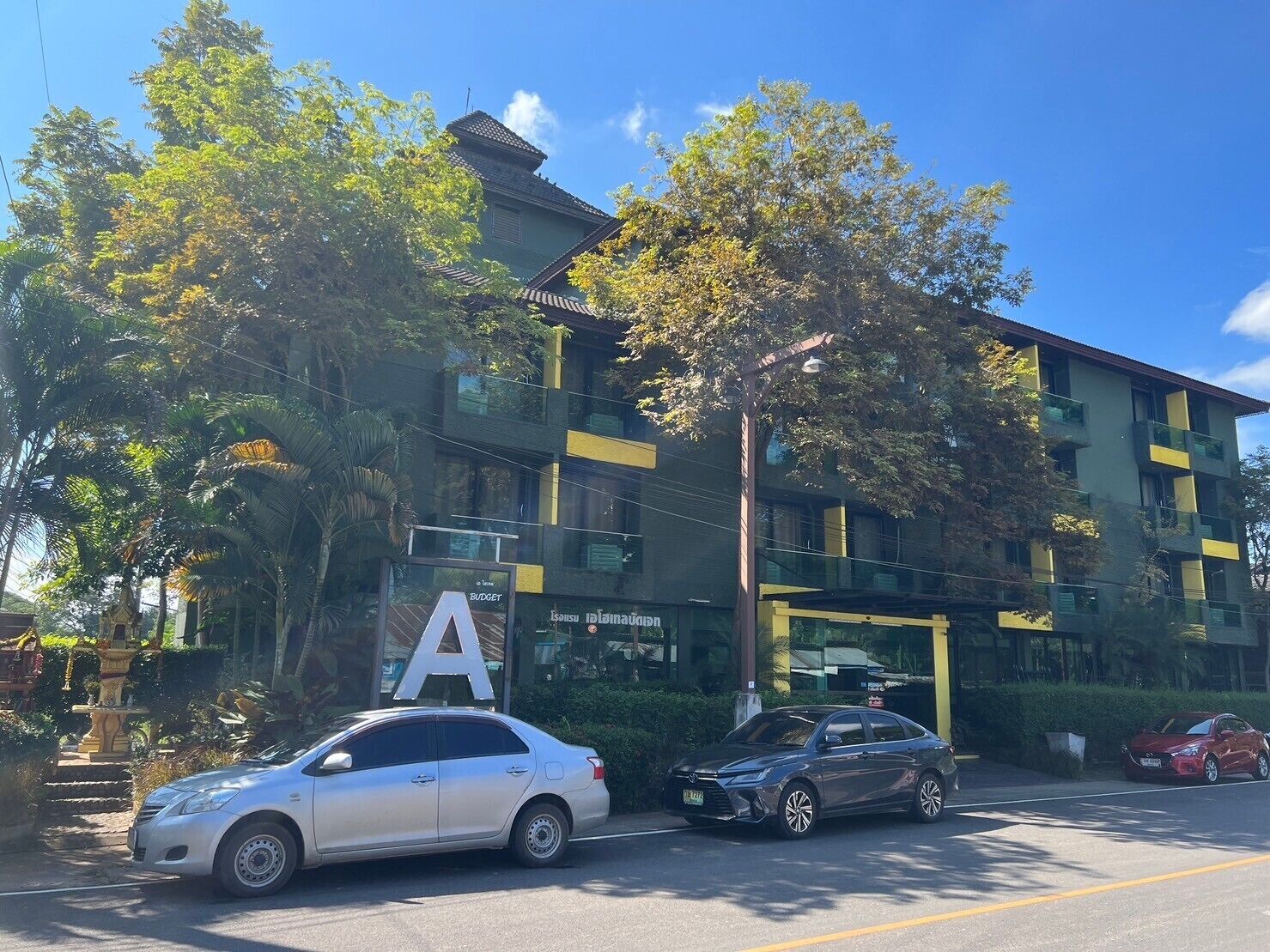 Un edificio con un cartel grande con la letra 'A', coches estacionados y árboles.