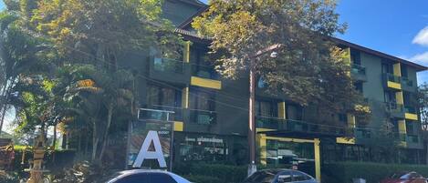 Un edificio con un cartel grande con la letra 'A', coches estacionados y árboles.