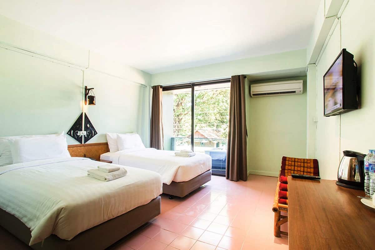 A hotel room with two beds, a dining table, a television, and a window with curtains.