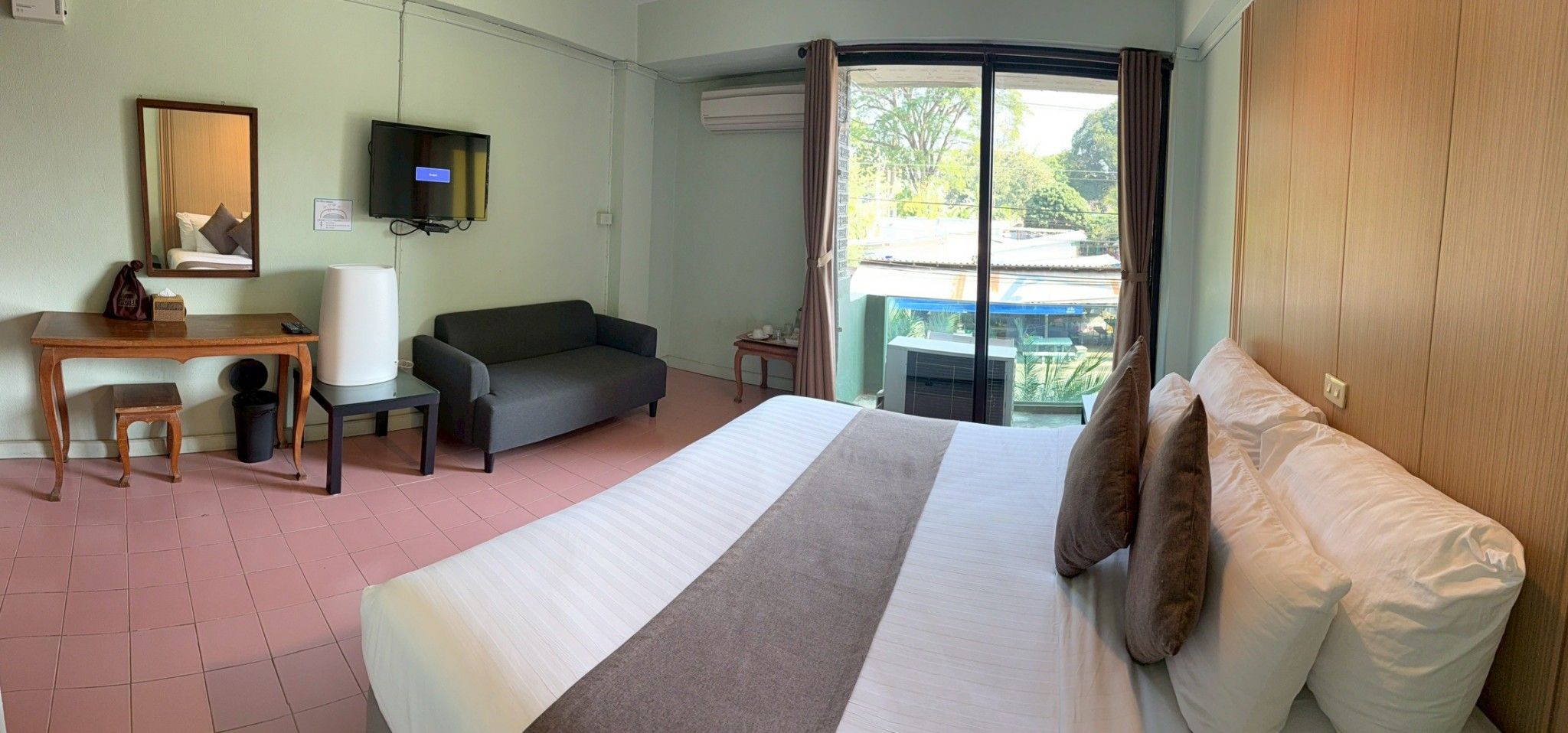 A hotel room with a bed, a sofa, a desk, a television, and a view of the outdoors.