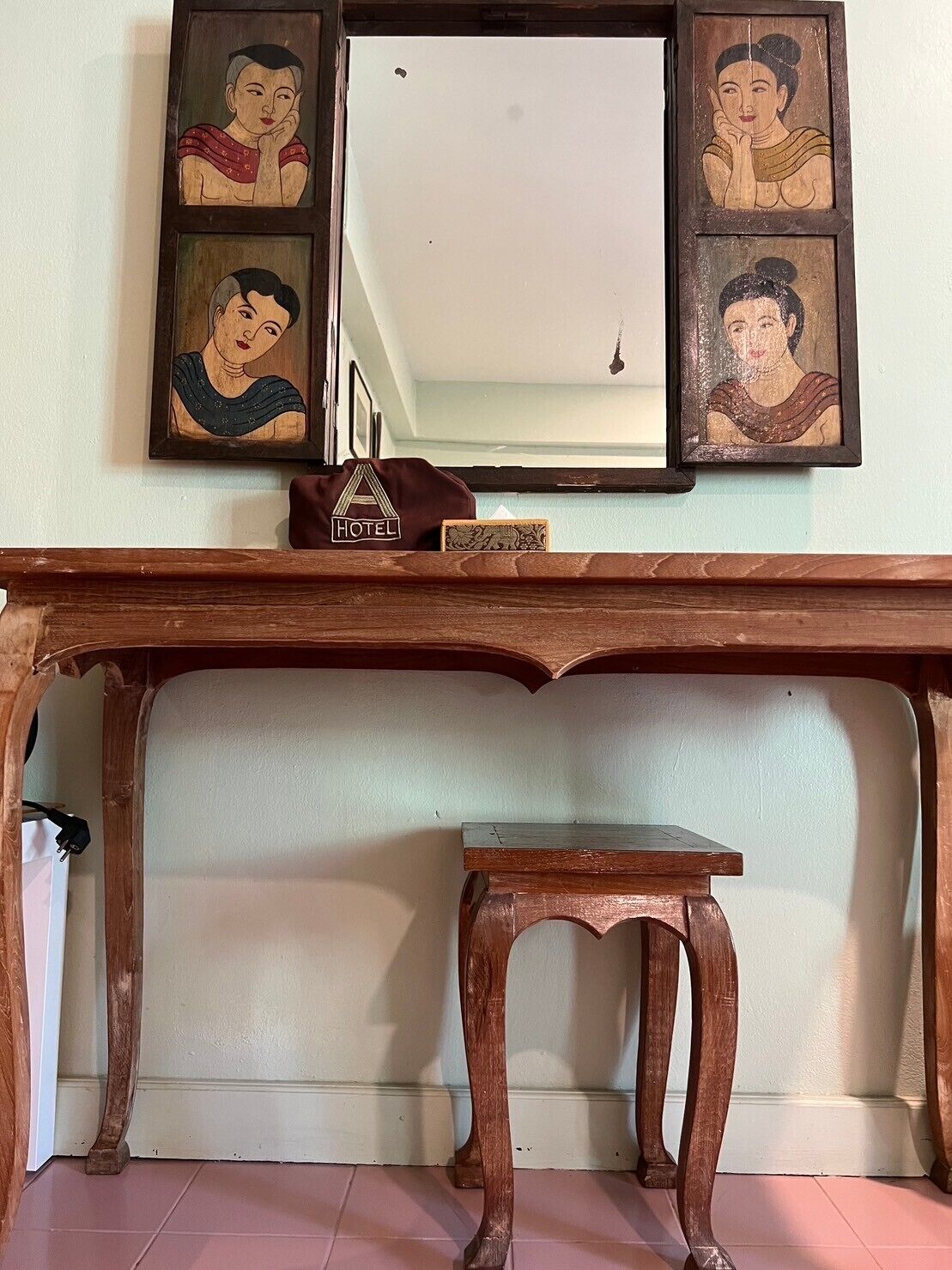 A wooden console table with a small stool in front, a framed mirror above, and a hotel sign on the table.