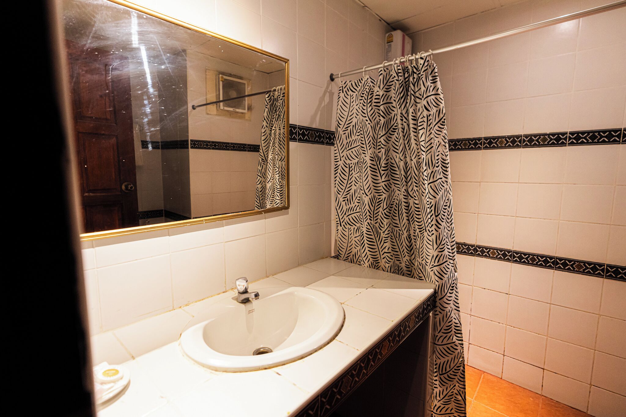 A bathroom with a white sink, a mirror, and a shower curtain with a leaf pattern.