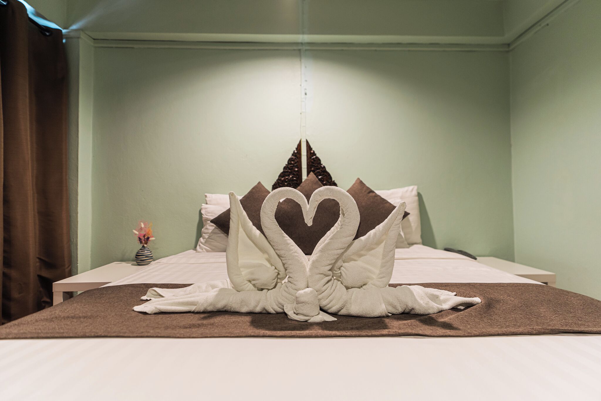 A neatly made bed with a heart-shaped pillow arrangement and a decorative towel centerpiece.