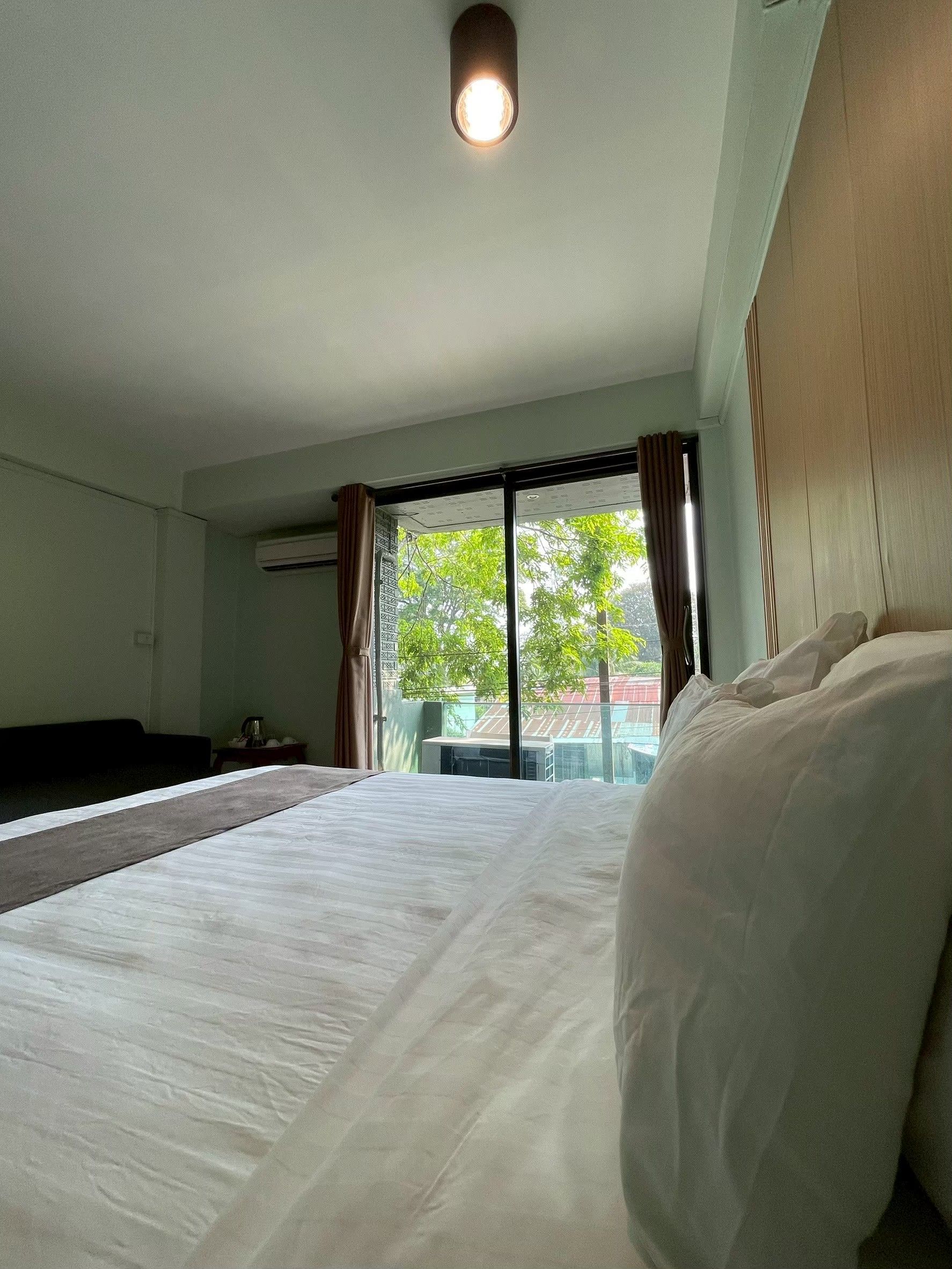 Hotellihuone, jossa on suuri sänky, ikkuna verhoilla ja näkymä puita ja rakennuksia ympäröivään maisemaan.