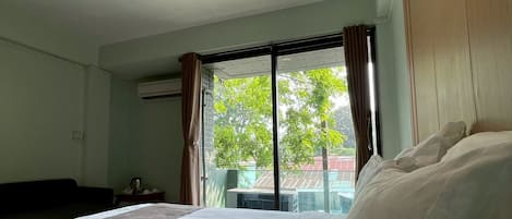 Hotellihuone, jossa on suuri sänky, ikkuna verhoilla ja näkymä puita ja rakennuksia ympäröivään maisemaan.