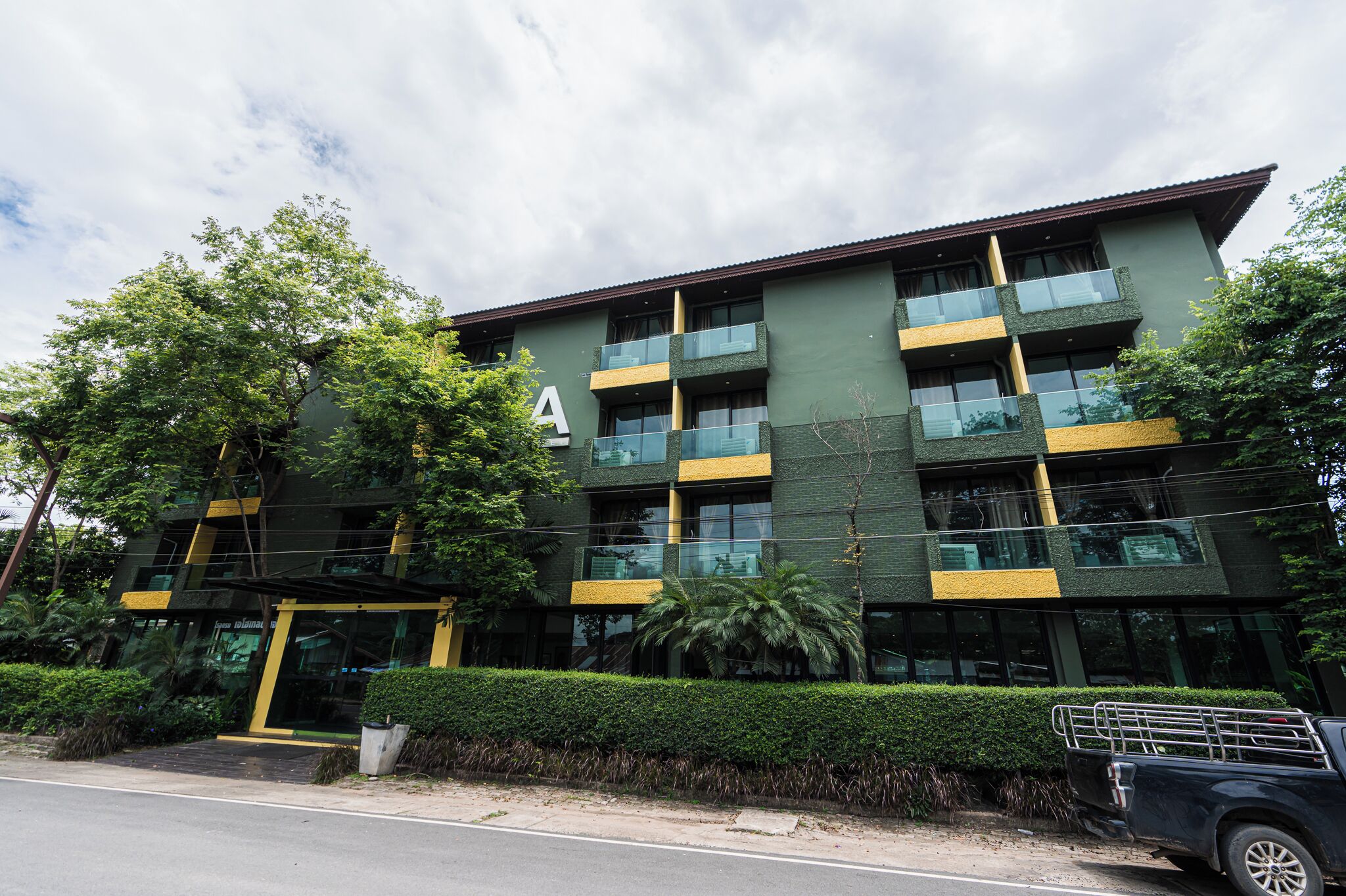 A multi-story building with a green facade, multiple balconies, and a large entrance.