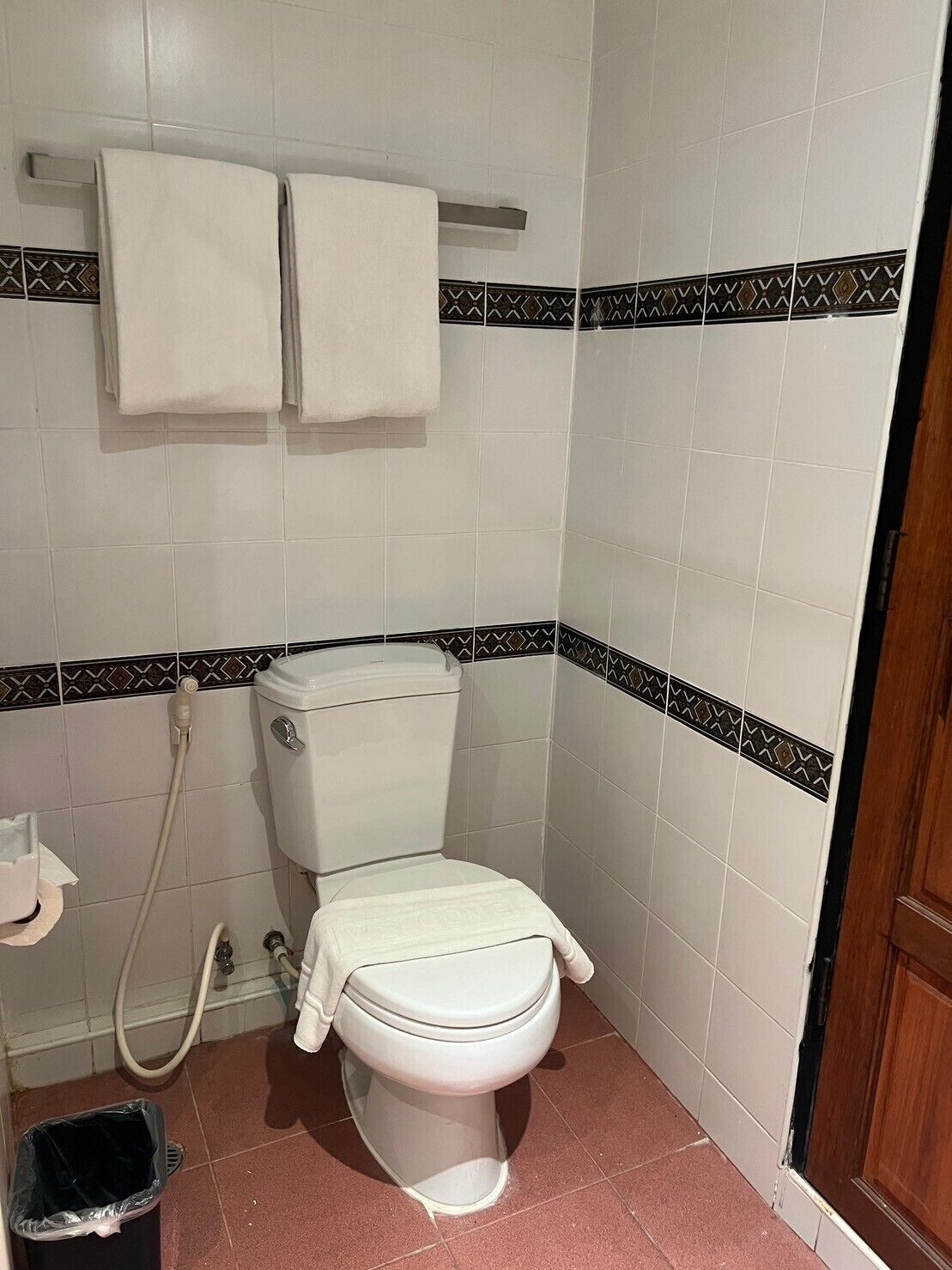A small bathroom with a toilet, a shower, and a trash bin.