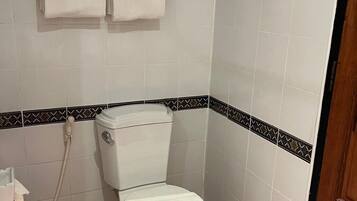 A small bathroom with a toilet, a shower, and a trash bin.