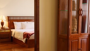 Una cama de madera con ropa de cama blanca, una mesita de noche con una lámpara y un armario de madera con puertas de cristal.