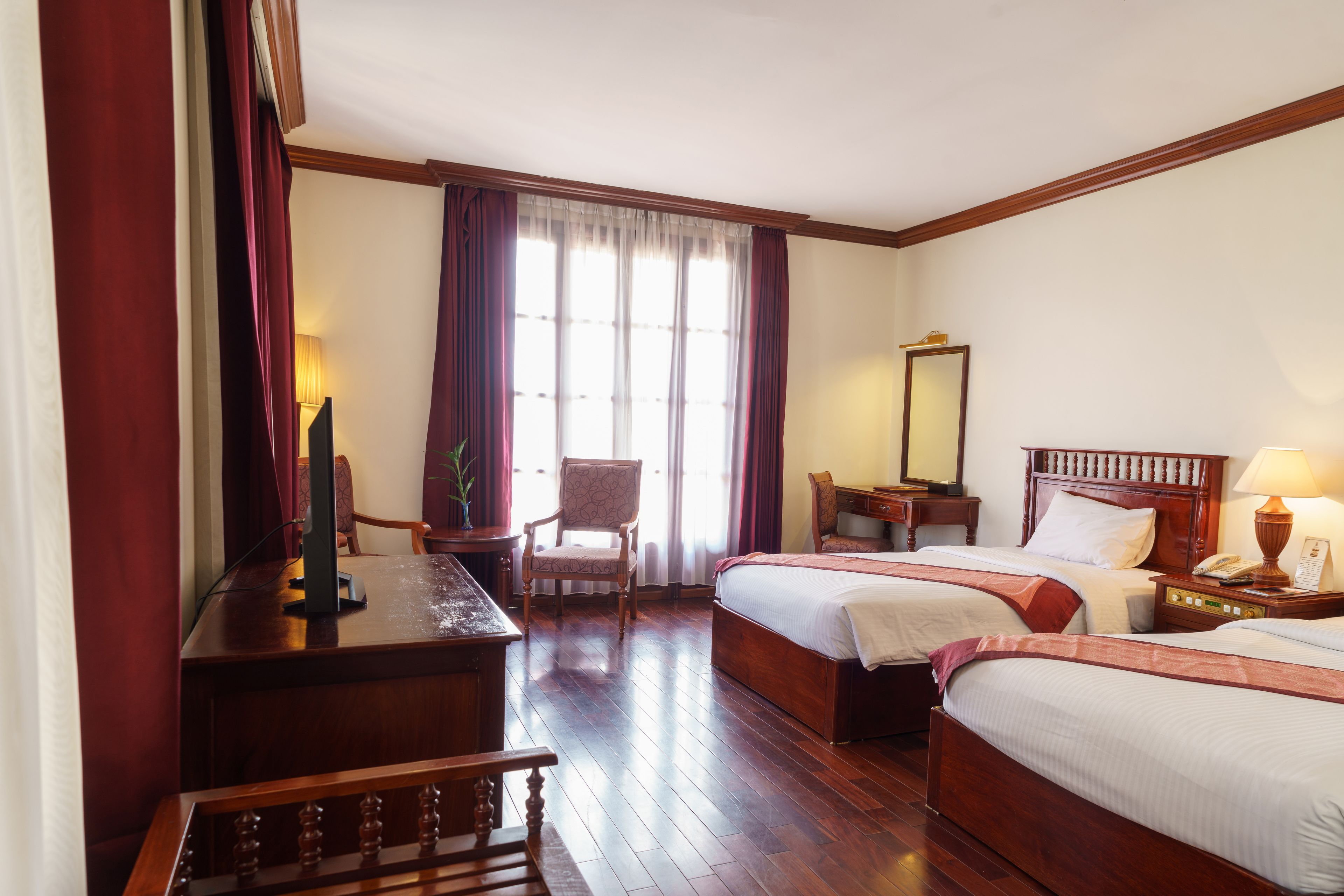 A hotel room with two beds, a desk, a chair, a mirror, and a window with curtains.