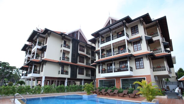 Un hotel de varios pisos con balcones, piscina y sillones de descanso.