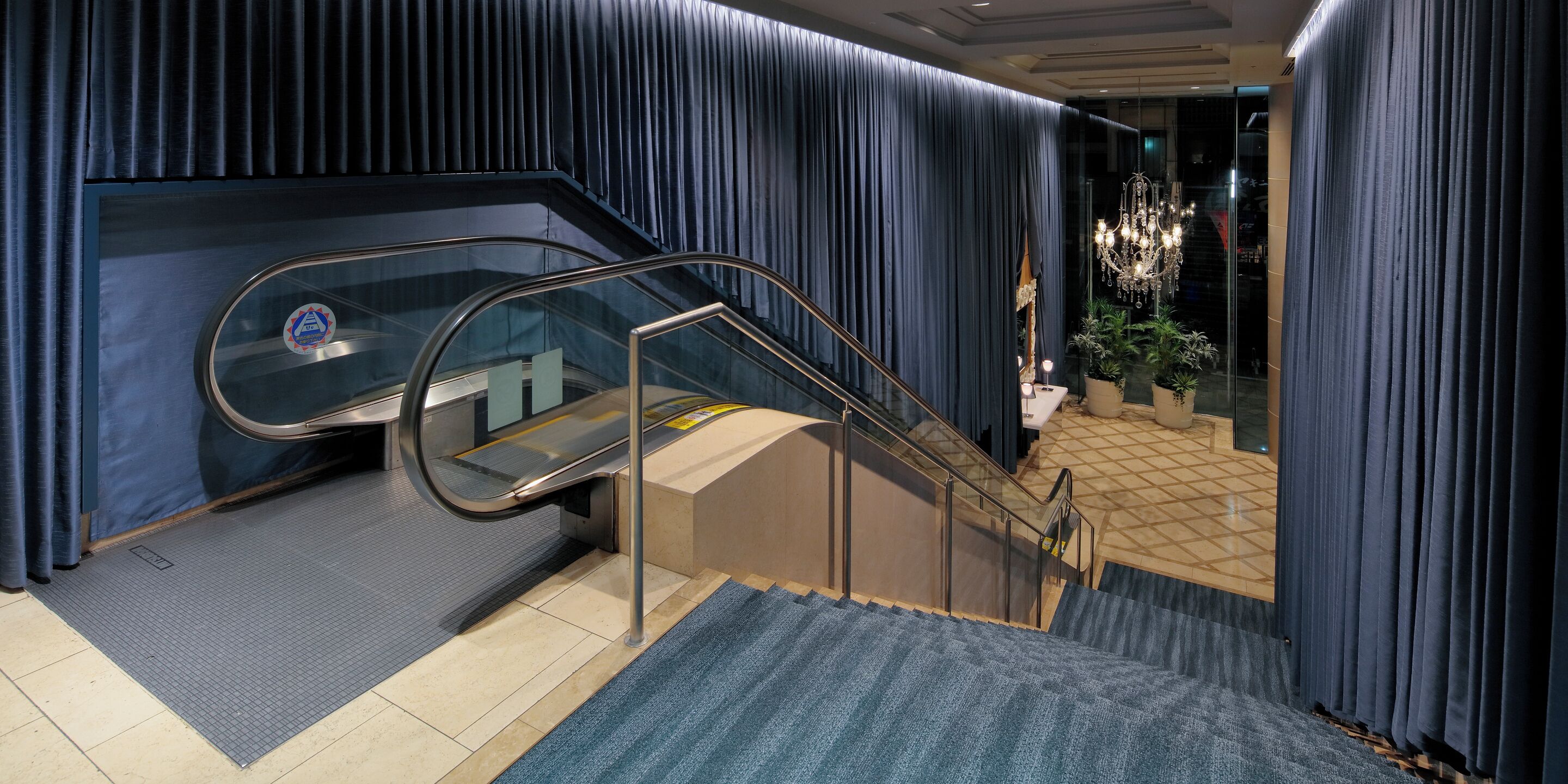 Un moderno vestíbulo de hotel con un ascensor de vidrio, una escalera y un candelabro.