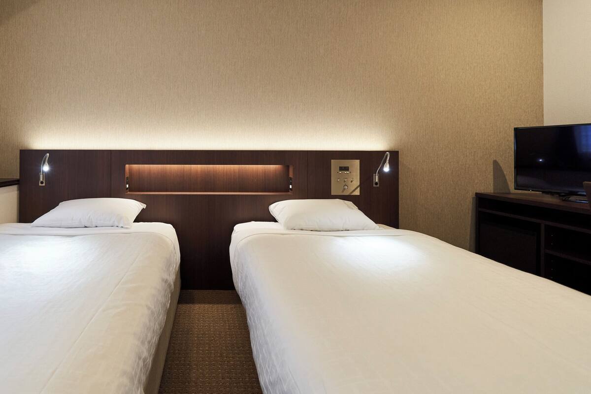 A hotel room with two single beds, a TV, and a wooden headboard with built-in lighting.