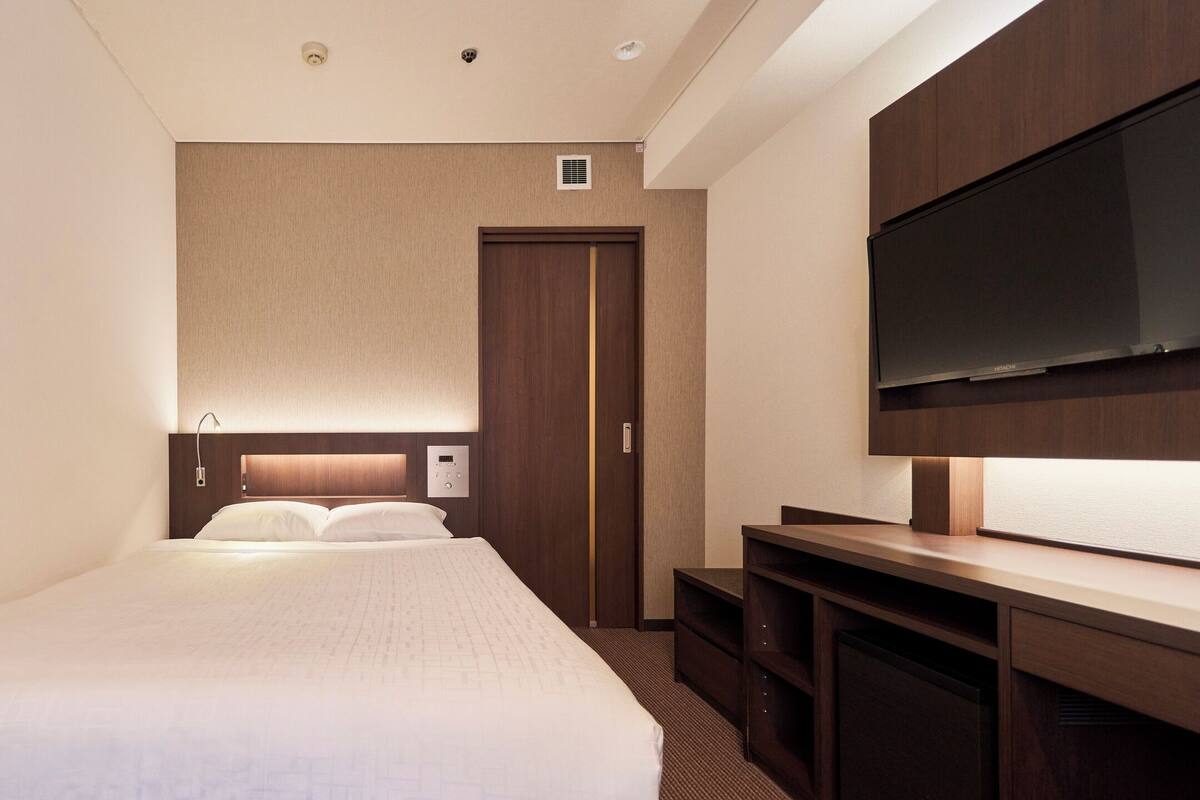 A hotel room with a bed, a TV, a wooden wardrobe, and a door.