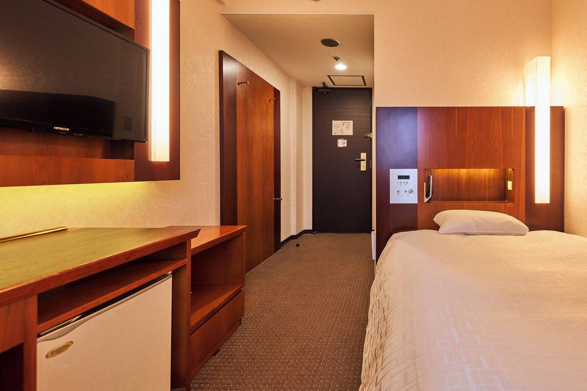 A hotel room with a bed, a desk, a television, and a bathroom door.