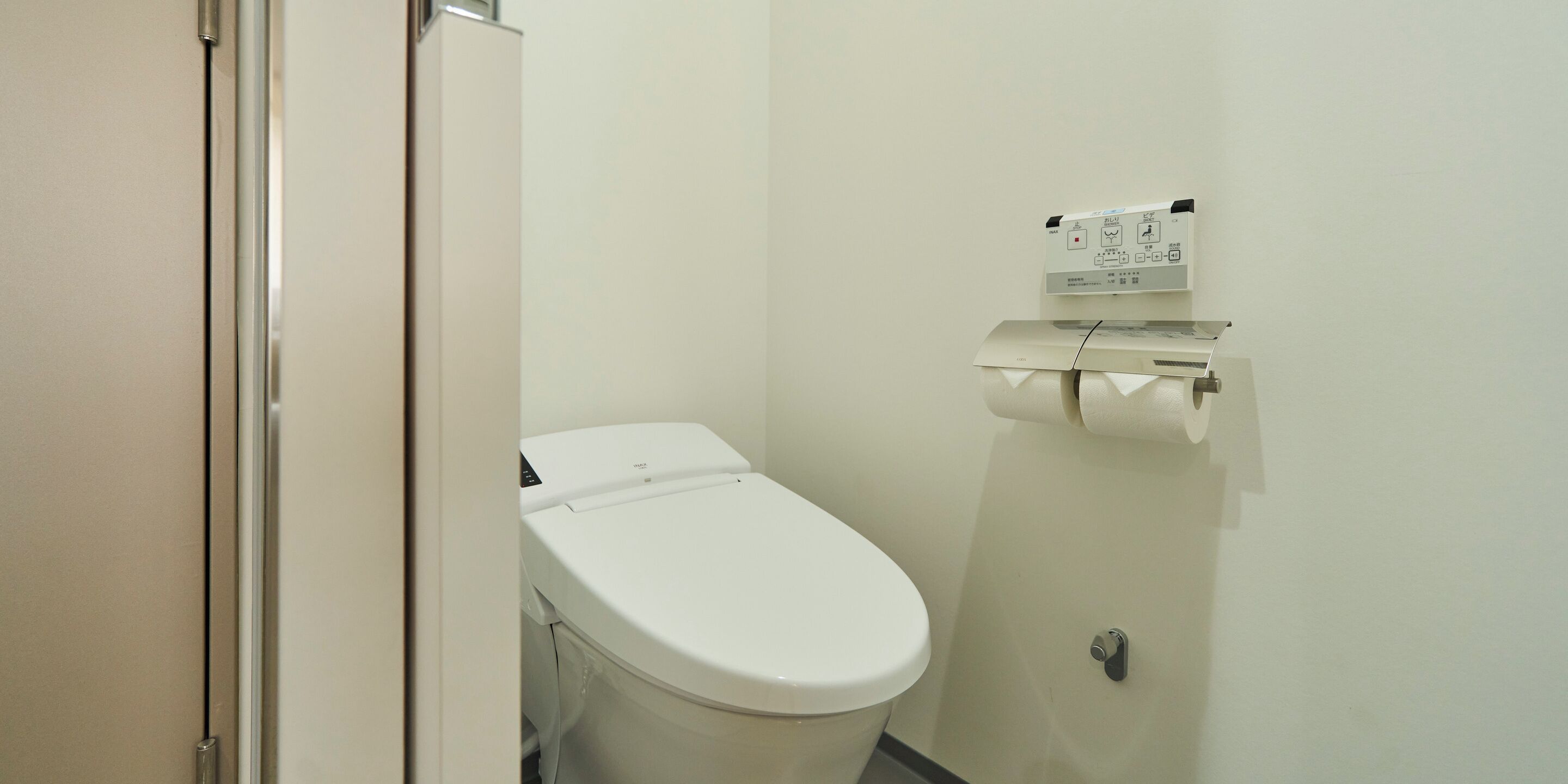 Un baño pequeño y limpio, con inodoro blanco, dispensador de toallas de papel y un rollo de papel higiénico en un soporte de pared.