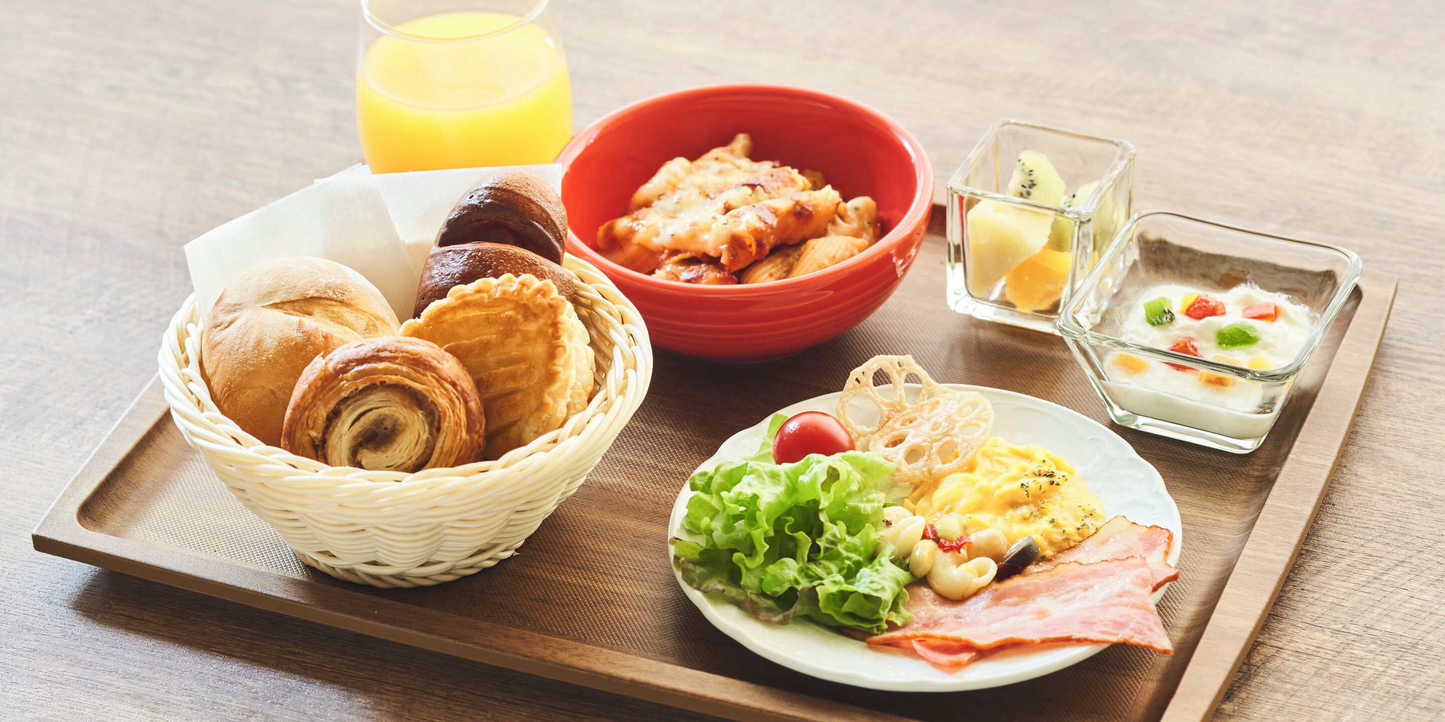 A breakfast tray with pastries, a bowl of food, a glass of orange juice, and a small dish with fruit.