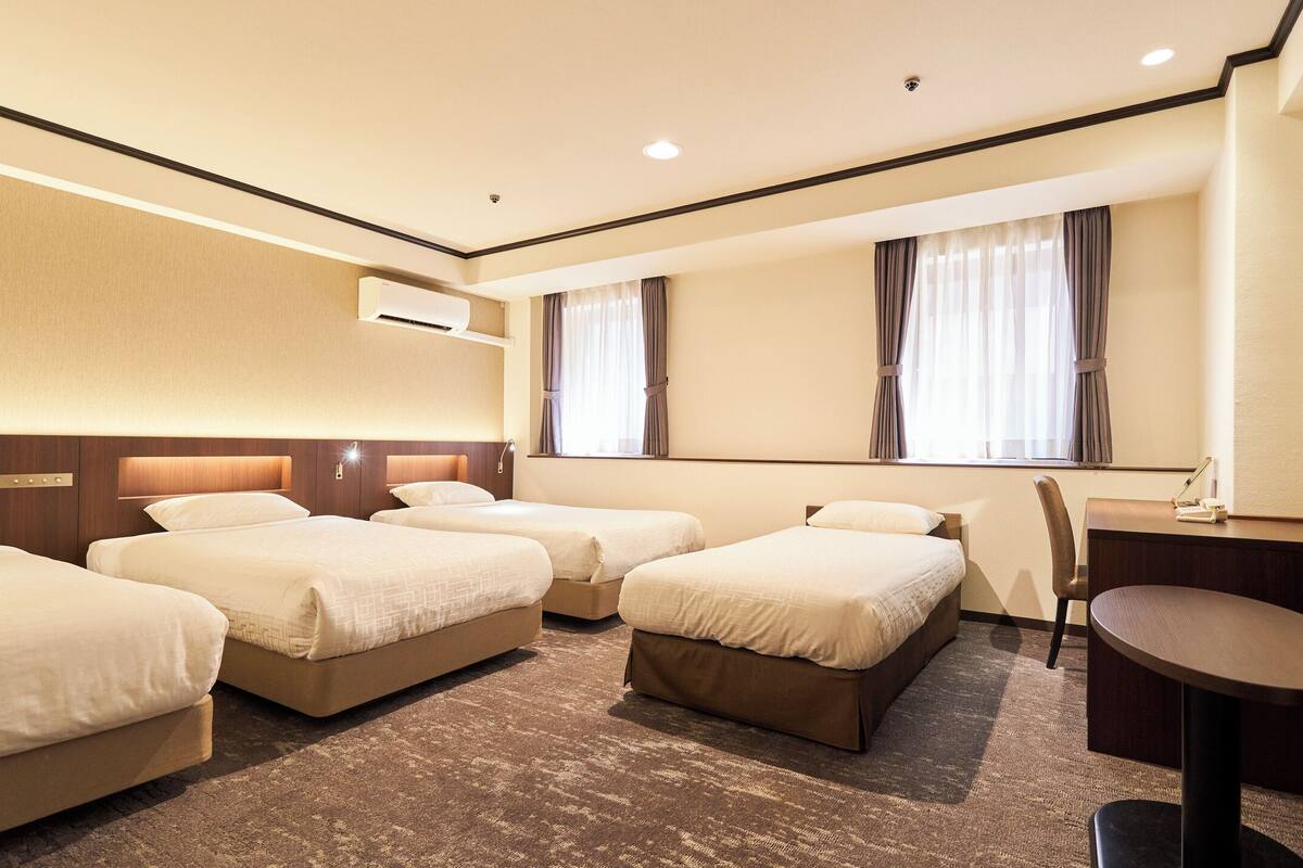 A hotel room with four beds, a desk, a chair, and a flat-screen TV.