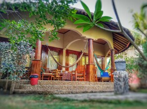 A wooden porch with a thatched roof, surrounded by lush greenery and a hammock. - Sejuk Cottages (Gili Air)