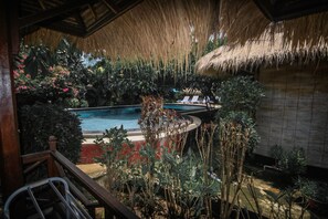 A pool area with a thatched roof, surrounded by lush tropical plants and a wooden deck. - Sejuk Cottages (Gili Air)