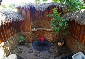 Un espacio exterior pequeño y cerrado, con techo de paja, una fuente central y plantas en macetas.