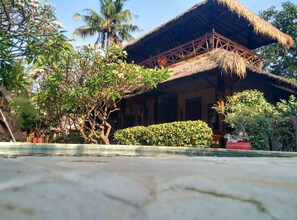 A traditional thatched-roof building with a wooden balcony, surrounded by lush greenery and a swimming pool. - Sejuk Cottages (Gili Air)