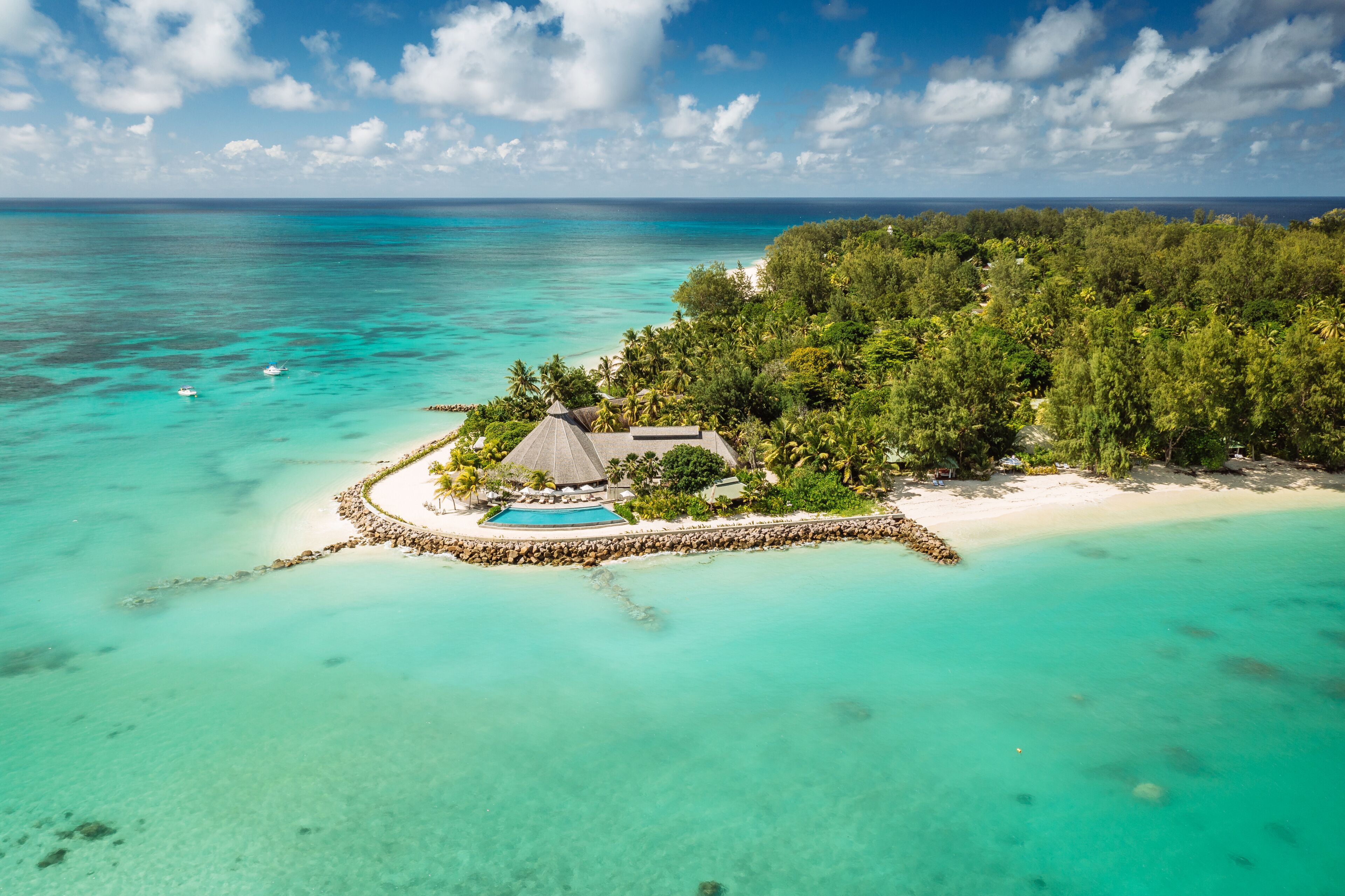 An aerial view of a tropical island with a swimming pool, a thatched-roof building, and lush greenery.