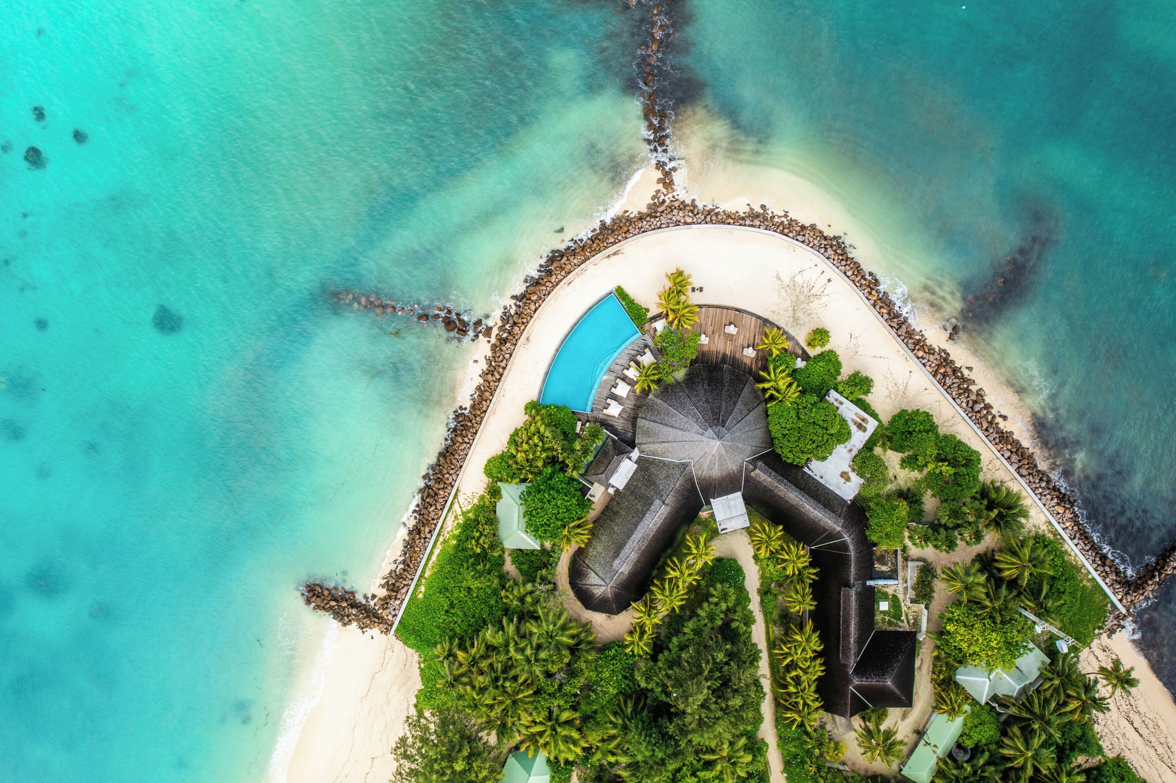 An aerial view of a resort with a swimming pool, palm trees, and a beach.
