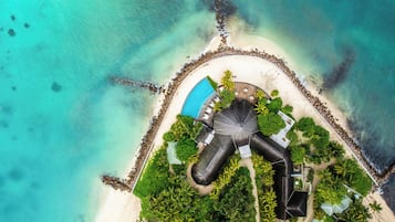 An aerial view of a resort with a swimming pool, palm trees, and a beach.