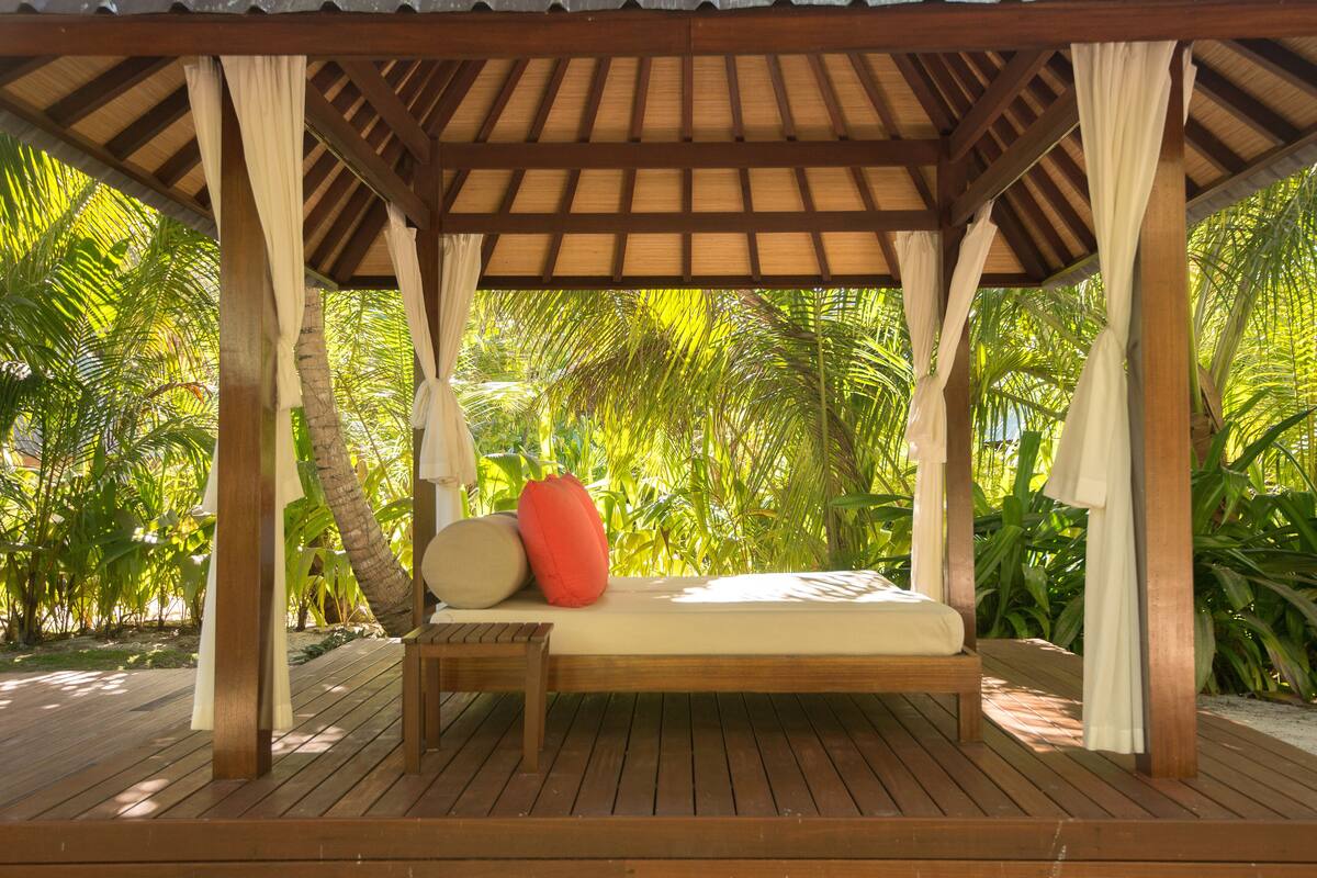 A wooden deck with a canopy, a single bed, and a red pillow.