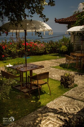 An outdoor patio with a table and chairs, surrounded by a garden with flowers and a view of the sea. - Anda Amed Resort (Karangasem)