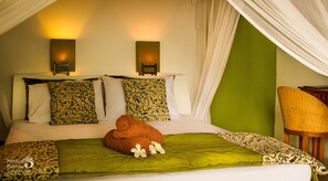 A bed with a green blanket, two patterned pillows, and a brown towel. There are two wall-mounted lights and a chair in the corner. - Anda Amed Resort (Karangasem)