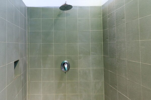 A shower area with a handheld showerhead and a fixed wall-mounted faucet.