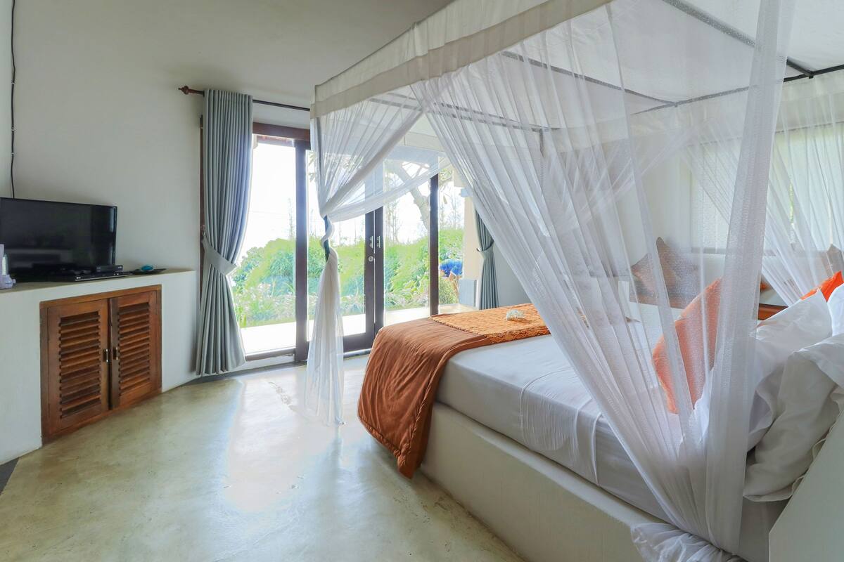 A bedroom with a bed, a television, and a sliding glass door leading to a balcony.